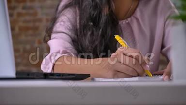 年轻忙碌的女孩在阁楼办公室里用笔记本电脑工作，打字，在笔记本上写纸条，在砖墙上写字